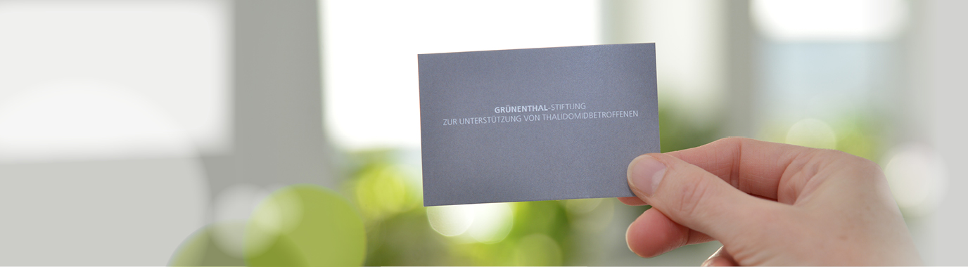 A hand holding a business card of the Grünenthal Foundation