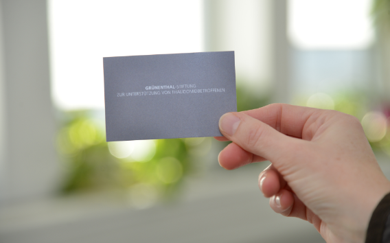 A hand holding a business card of the Grünenthal Foundation